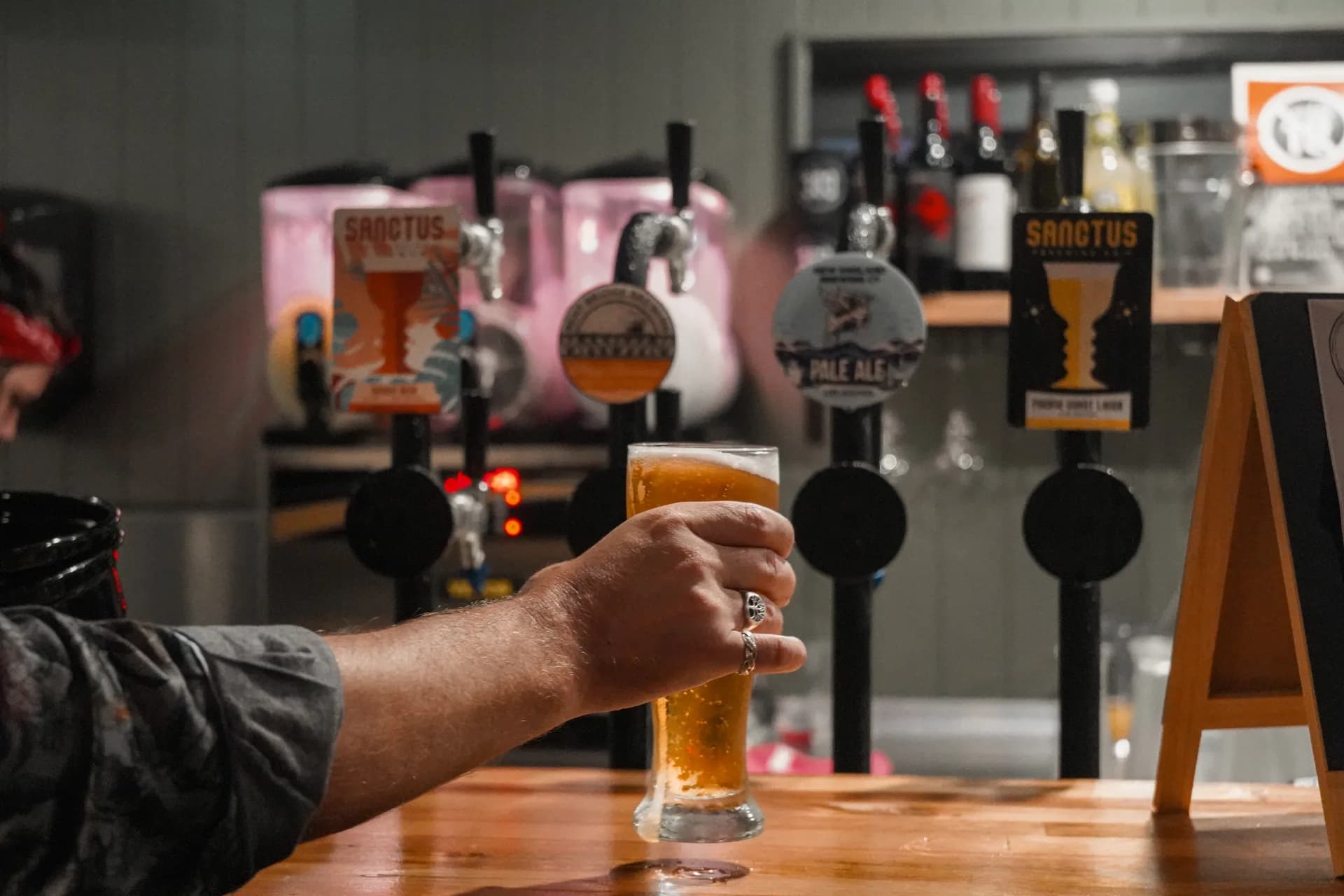 A hand setting a schooner of cold beer down on the timber bar in front of a row of craft beer taps.