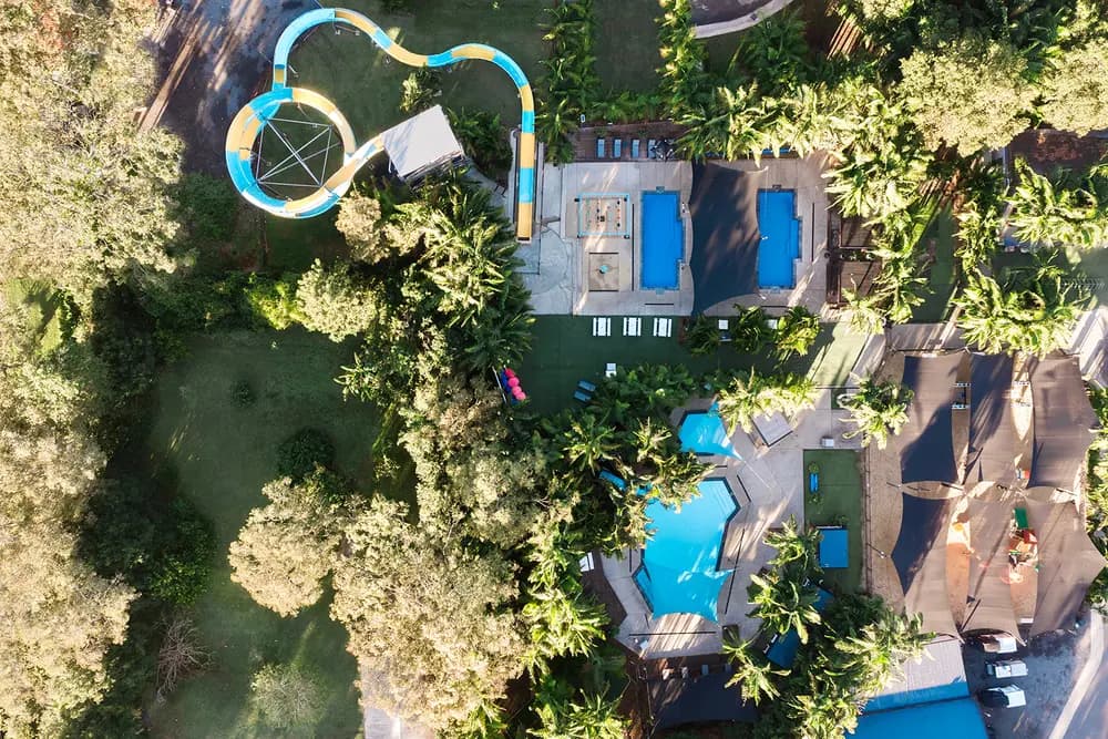 Aerial view of the resort's water park: the blue and yellow waterslide, swimming pools and splash area set among palms and lawn.