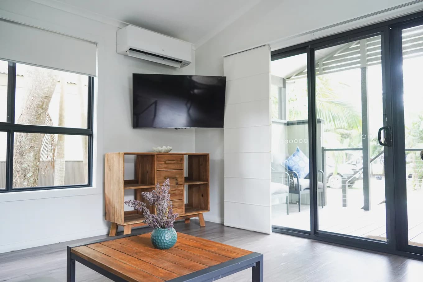 Living area in the accessible cabin, with a wall-mounted TV, a timber sideboard and wide sliding doors opened onto the deck.