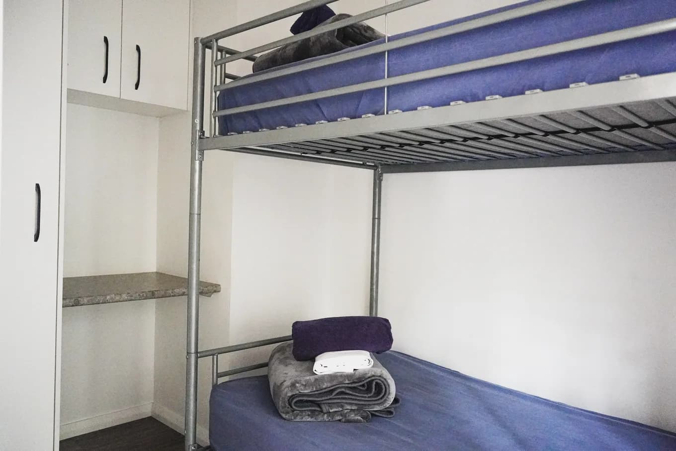 Steel-framed bunk in the accessible cabin, the lower bed made up with folded towels, with open storage shelving alongside.