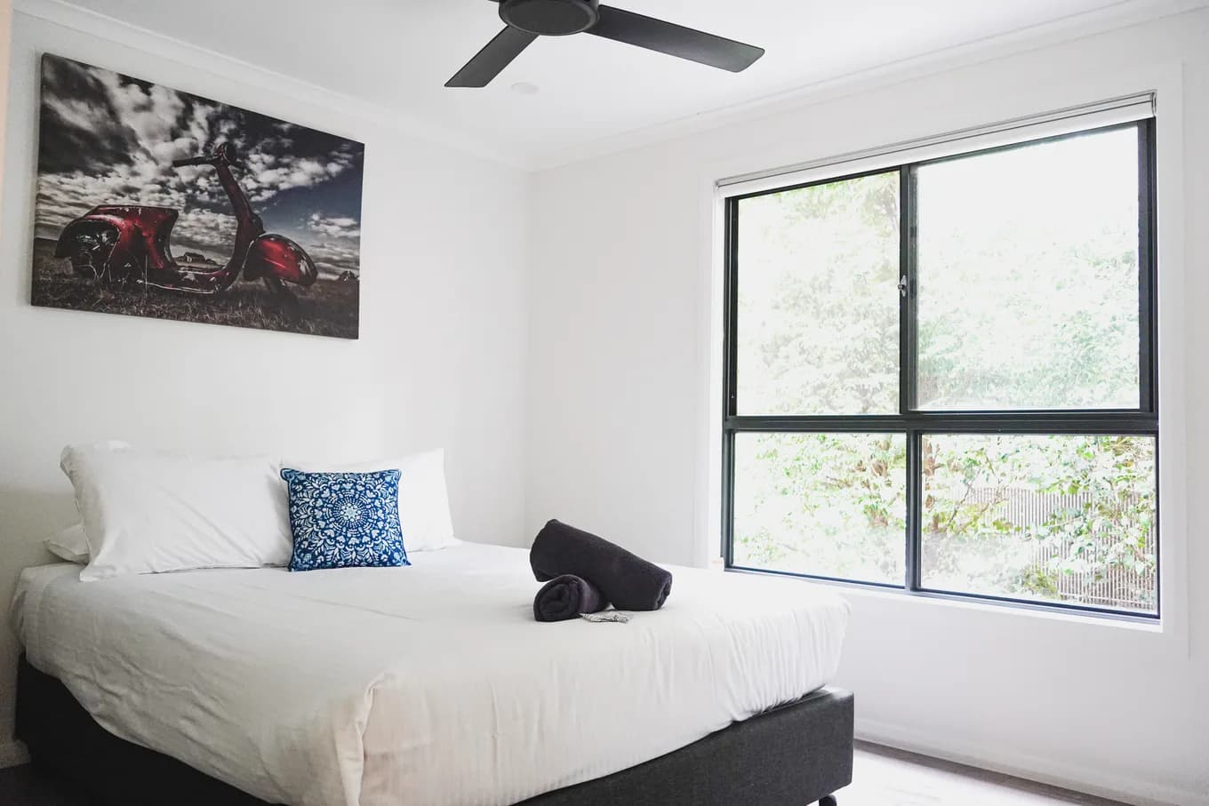 Queen bedroom in the accessible cabin, made up in white with a patterned cushion, a ceiling fan overhead and a window onto the trees.