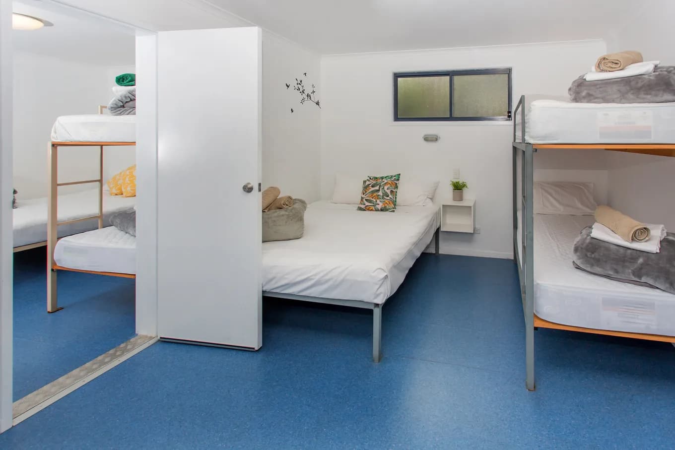 Inside a Beach Hut: a double bed and two sets of bunks on a blue vinyl floor, with the door open to outside.