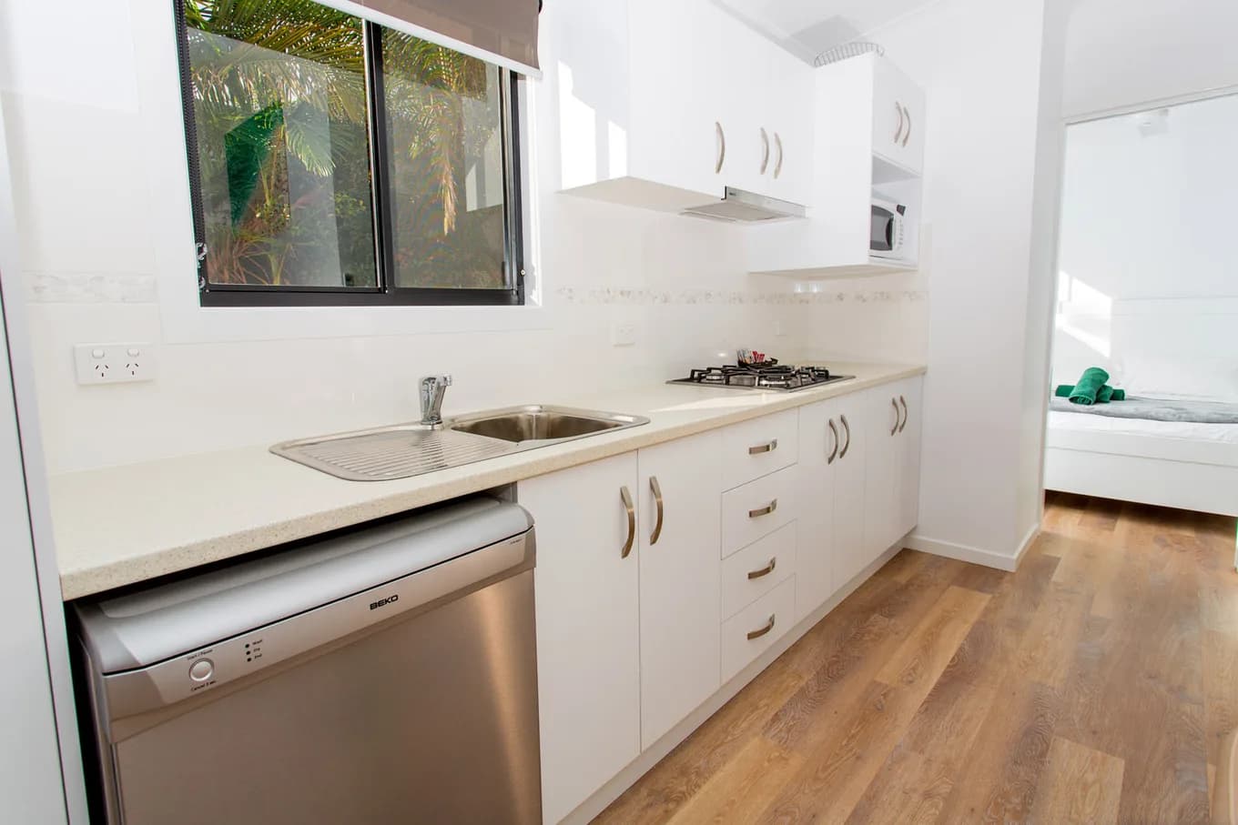Galley kitchen in the executive cabin, with a stainless sink, gas cooktop, dishwasher and white cabinetry under a window.