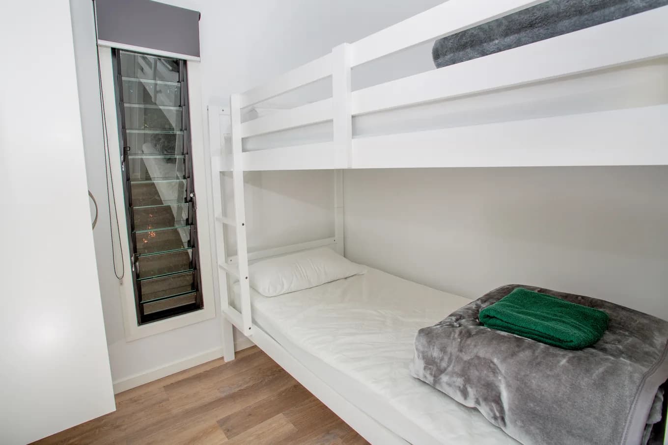 White timber bunk in the executive cabin, the lower bed made up in white with a grey throw and a folded green towel.