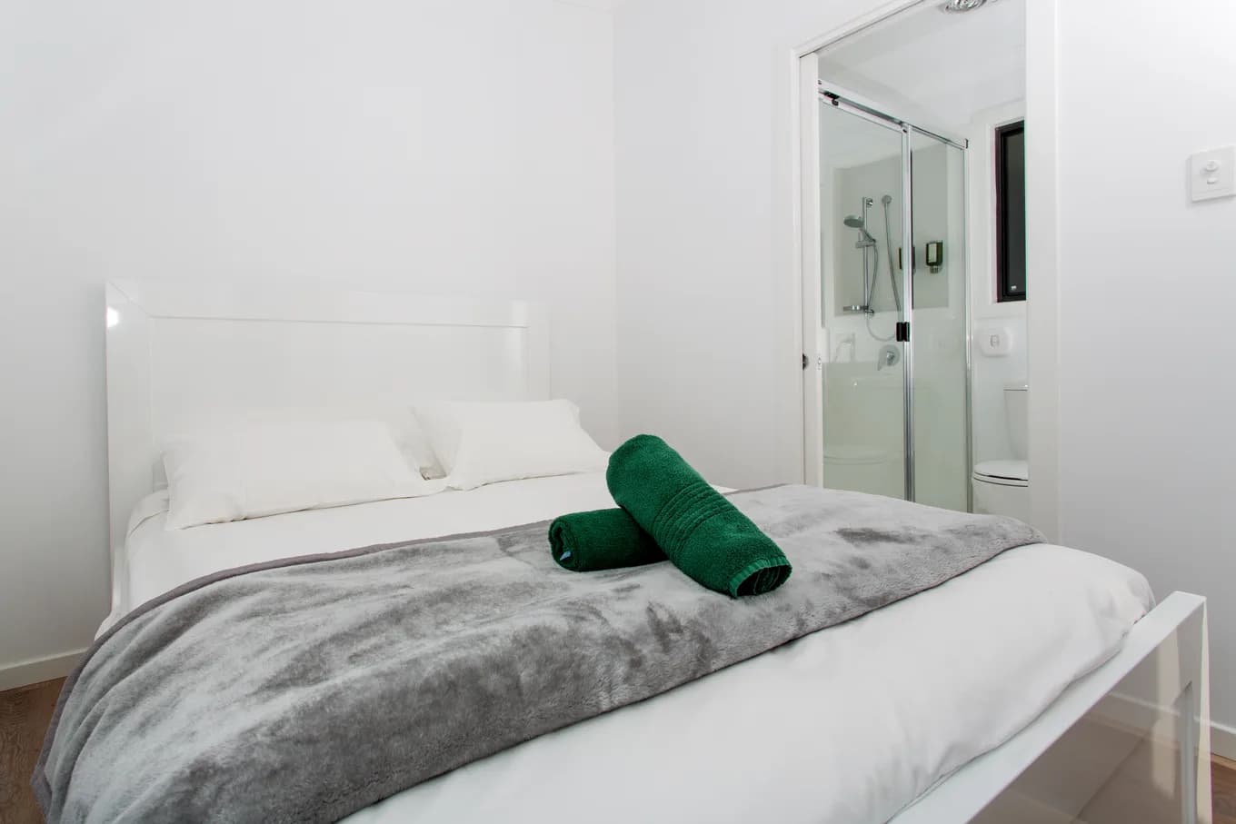 Queen bedroom in the executive cabin, made up in white with a grey throw and green rolled towels, and the ensuite shower through the open doorway.