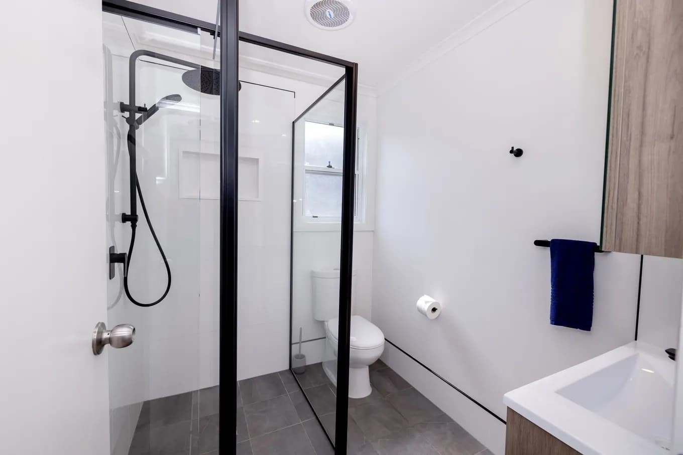 Bathroom in the Five Bedroom Luxury Riverview Villa: a glass-screened walk-in shower with a rain head, a toilet and a timber-fronted vanity on grey tiled floor.