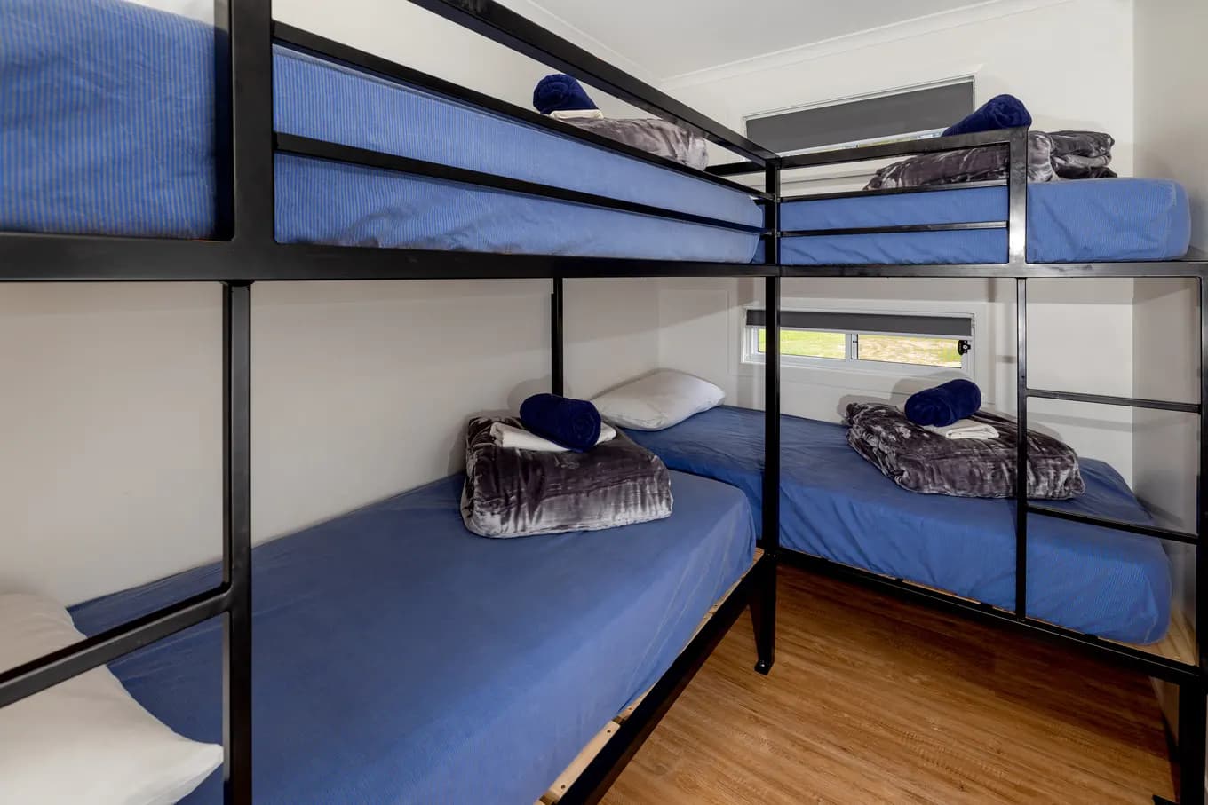 Bunk room sleeping four, with two black steel bunk beds made up in blue linen and a high window.