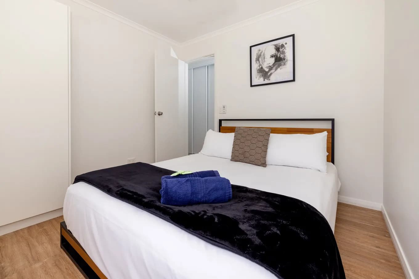 Queen bedroom in the villa, with a timber and black steel bedhead, white linen under a navy throw, and framed artwork above the bed.