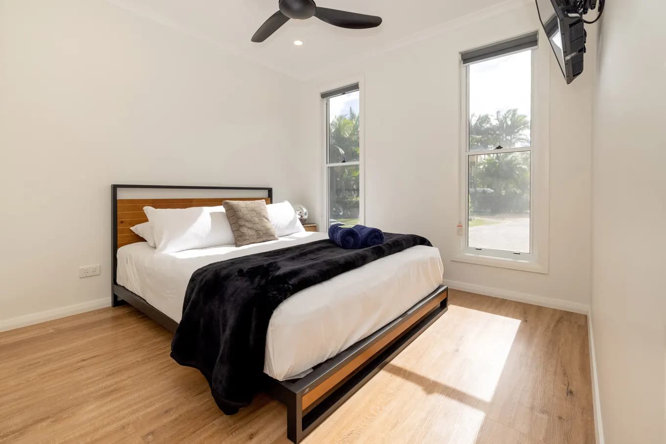Queen bedroom in the villa with a ceiling fan, a wall-mounted TV and two windows looking out to palms and the garden.