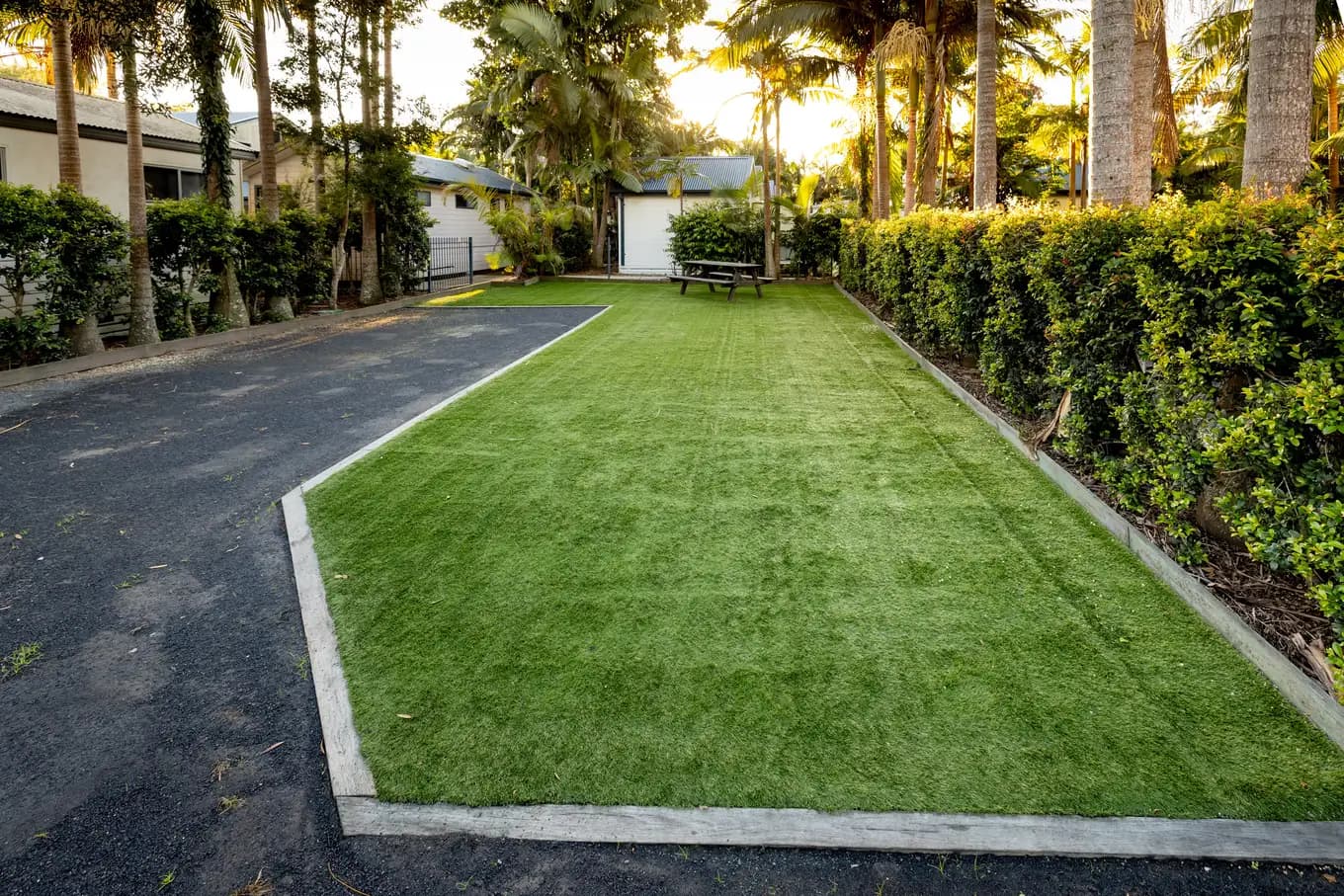 Long drive-through powered turf site, with a sealed driveway down one side and a clipped hedge along the other.