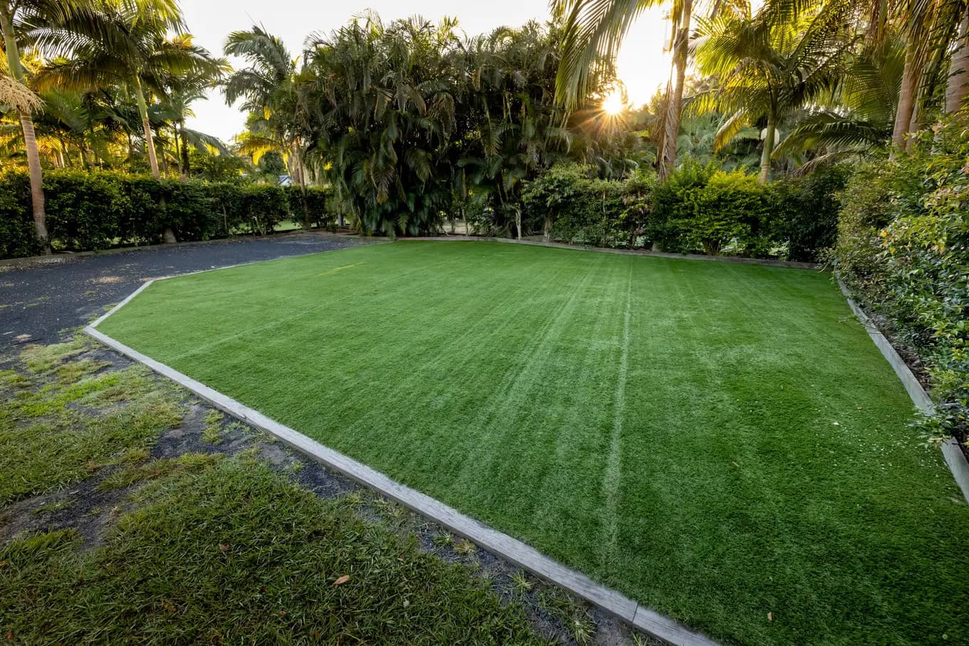 Golden-hour sun breaking through the palms over an empty powered turf site.