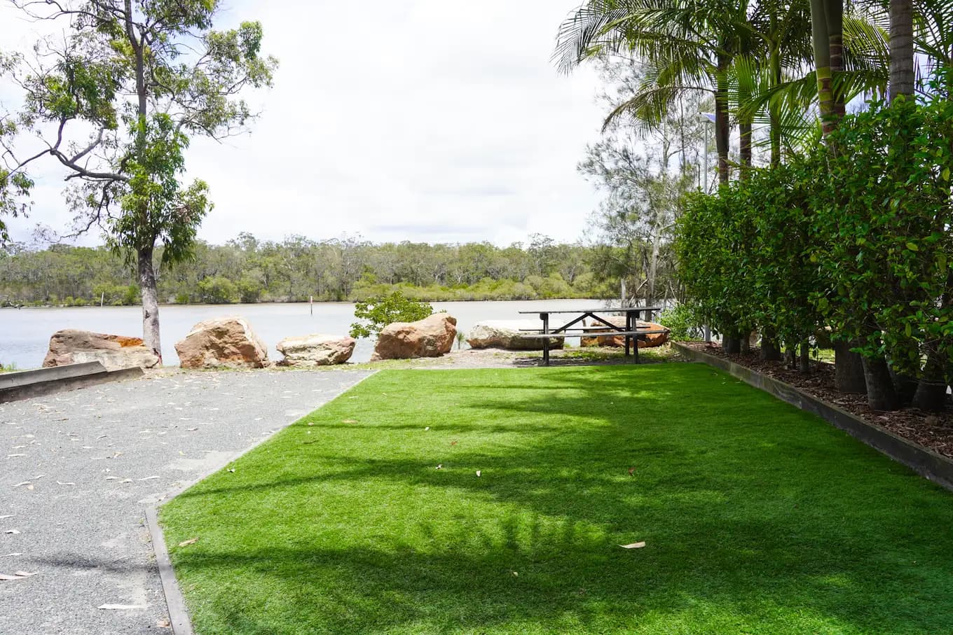 Turf pad at a riverfront tent site, edged with a hedge, the picnic table and the river directly out front.