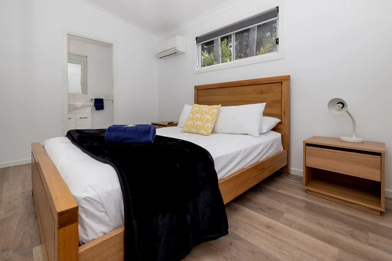 Master bedroom in the three bedroom villa, with a timber bedhead, white linen under a black throw, a bedside lamp, and a doorway through to the ensuite.