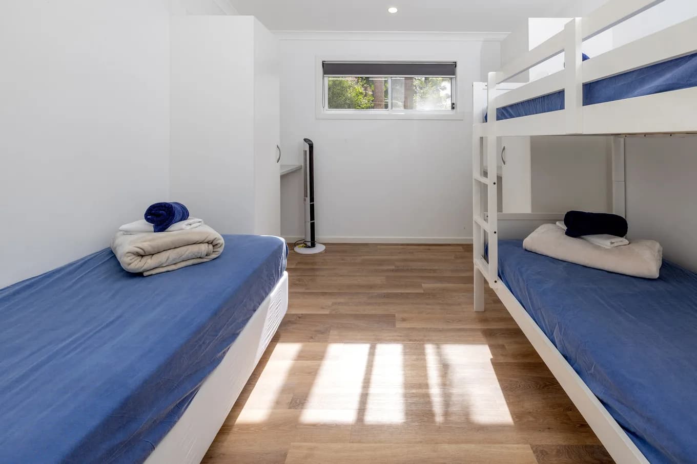 Bunk room in the three bedroom villa, with three single beds made up in blue and towels folded on the lower bunks.