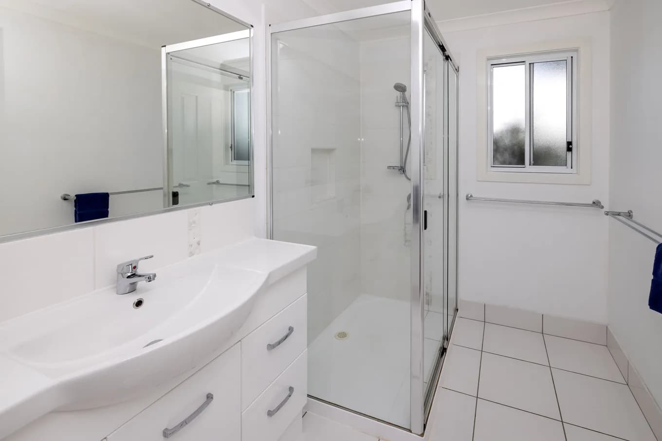 Main bathroom in the three bedroom villa, with a white vanity and mirror, a glass shower recess and white tiled floors.
