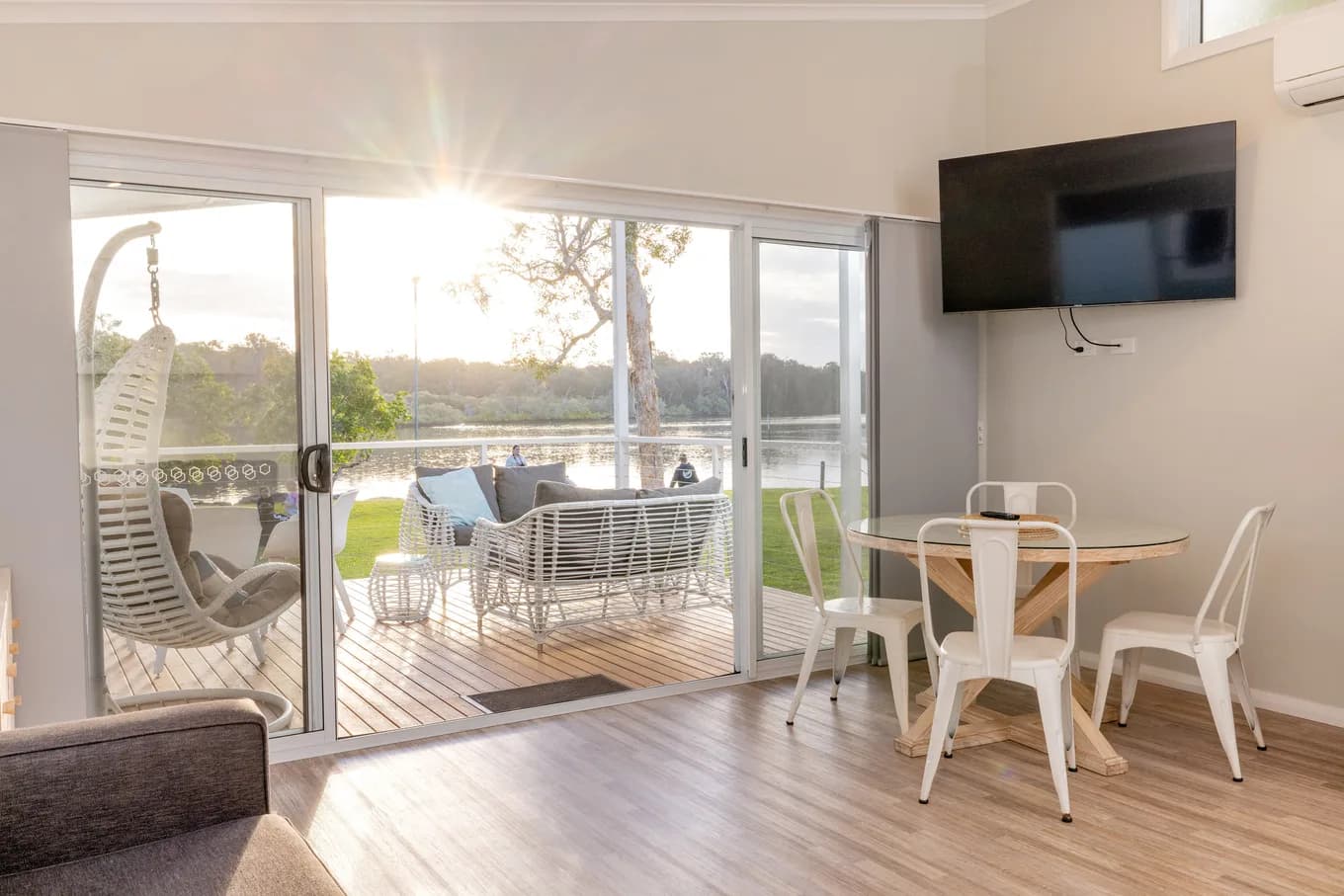 Late sun streaming through the villa sliding doors into the living and dining area, with the hanging chair and outdoor lounges on the deck beyond.